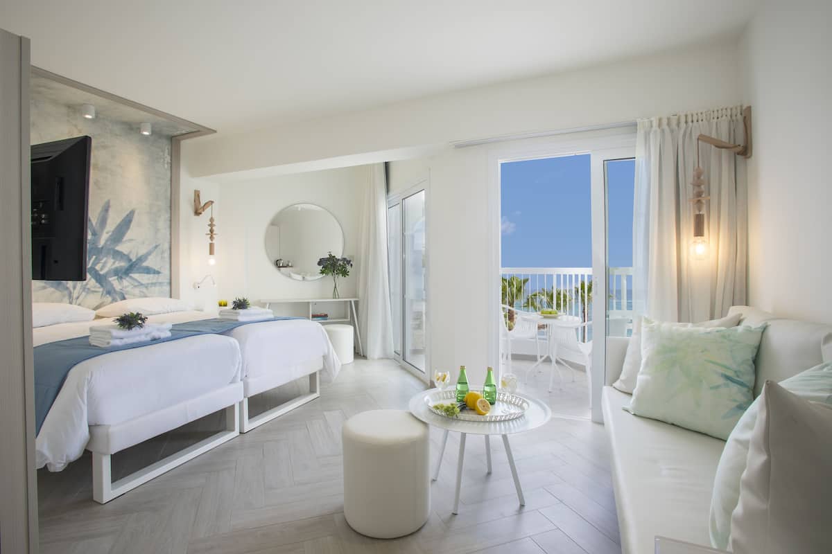 A modern hotel room with a balcony, a bed, a sofa, and a small table with drinks.