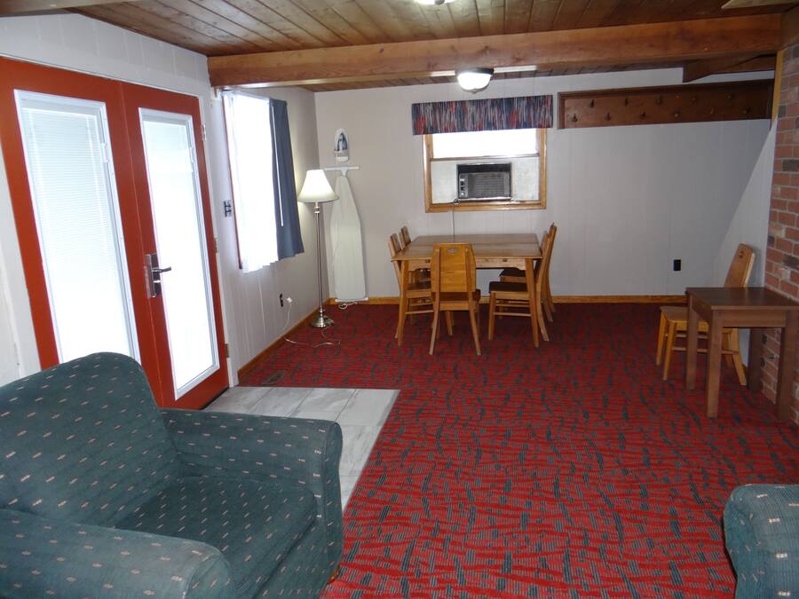 A room with a wooden ceiling, a dining table with chairs, a sofa, and a patterned carpet.