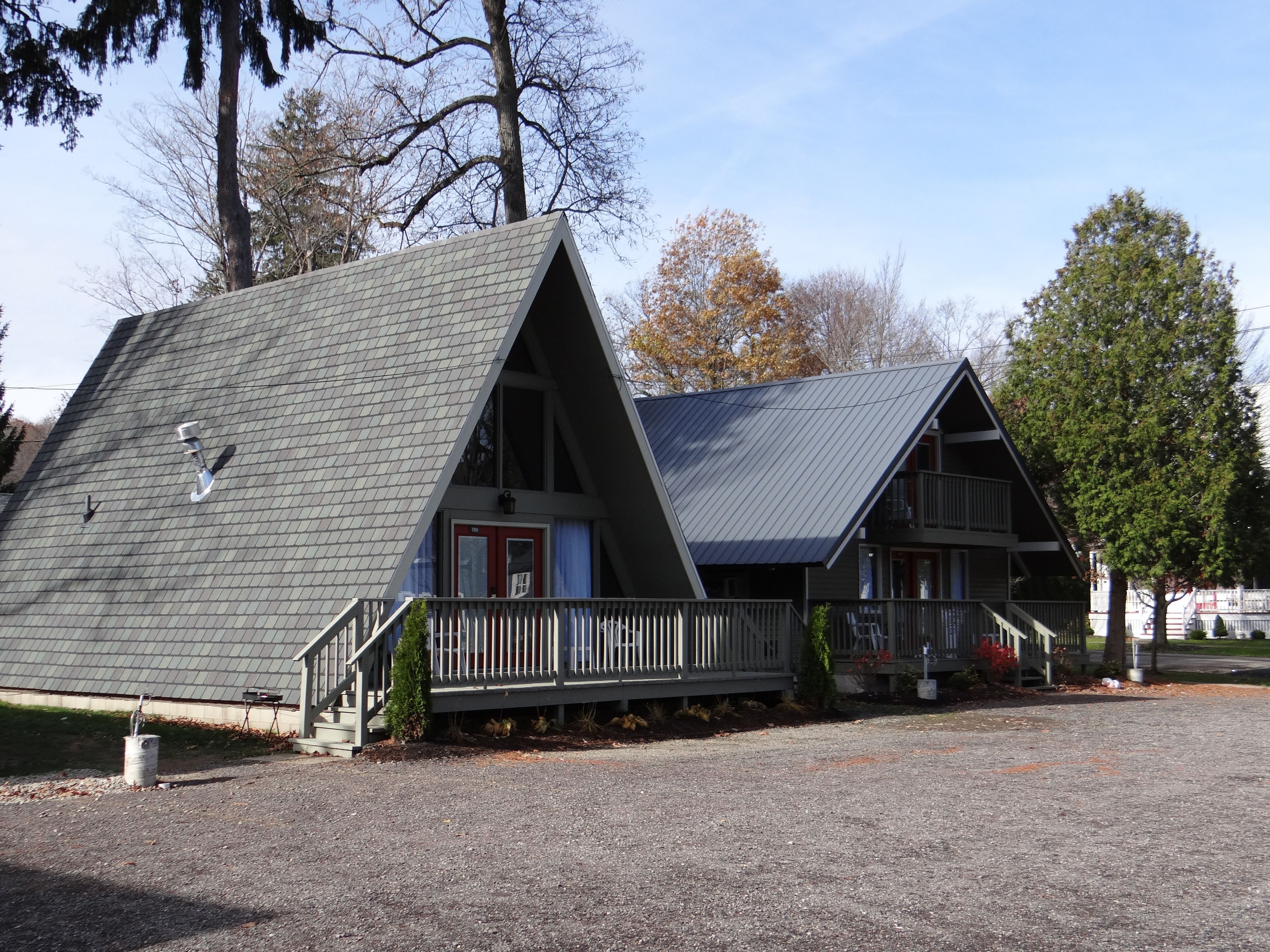A two-story cabin with a sloped roof, a front porch with a railing, and a red door.