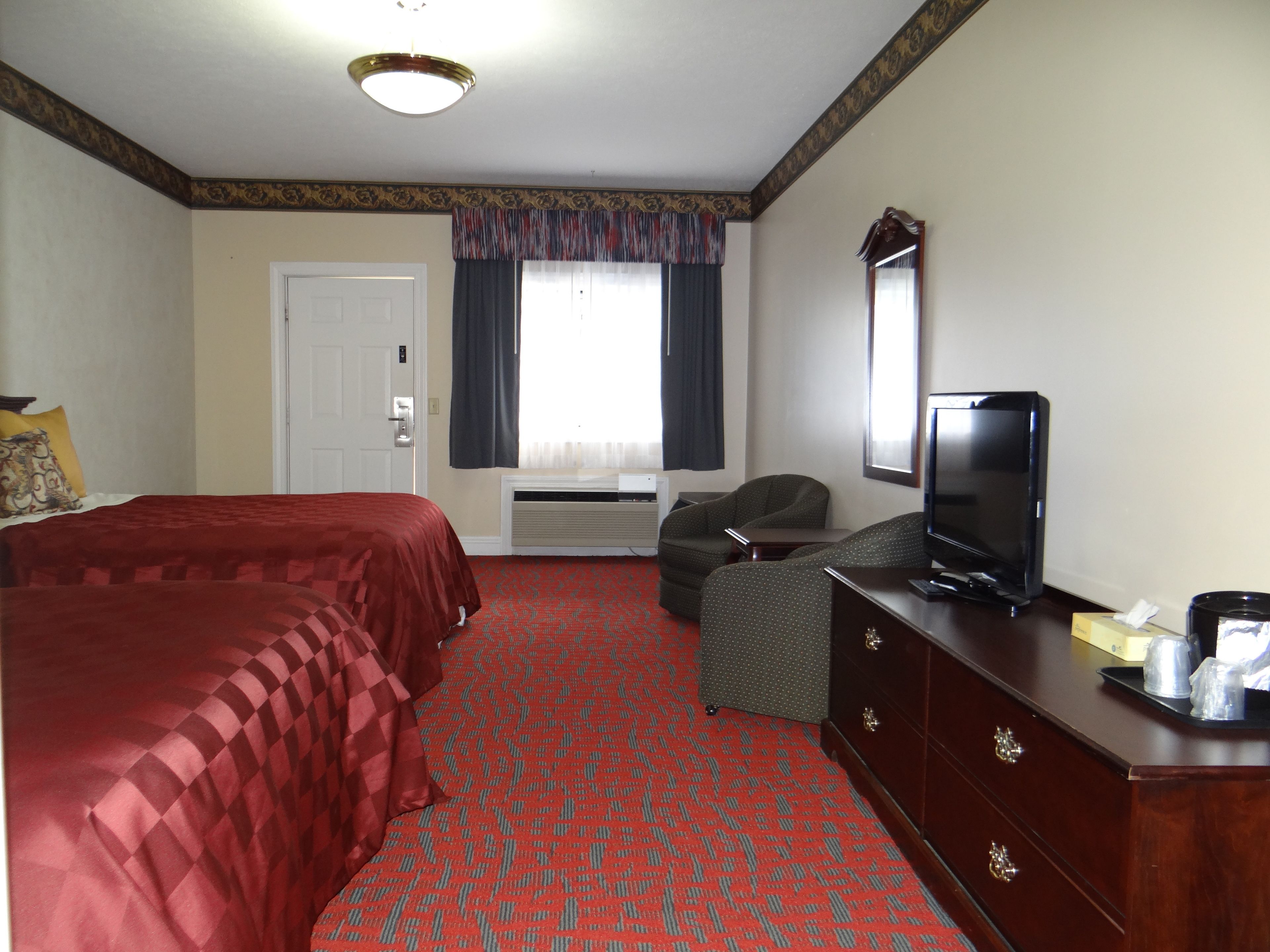 A hotel room with a bed, a sofa, a TV, a dresser, and a window with curtains.