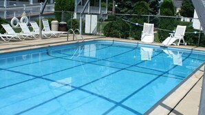Una piscina con agua cristalina azul, rodeada de sillas reclinables blancas y una valla metálica.