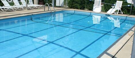A swimming pool with clear blue water, surrounded by white lounge chairs and a metal fence.