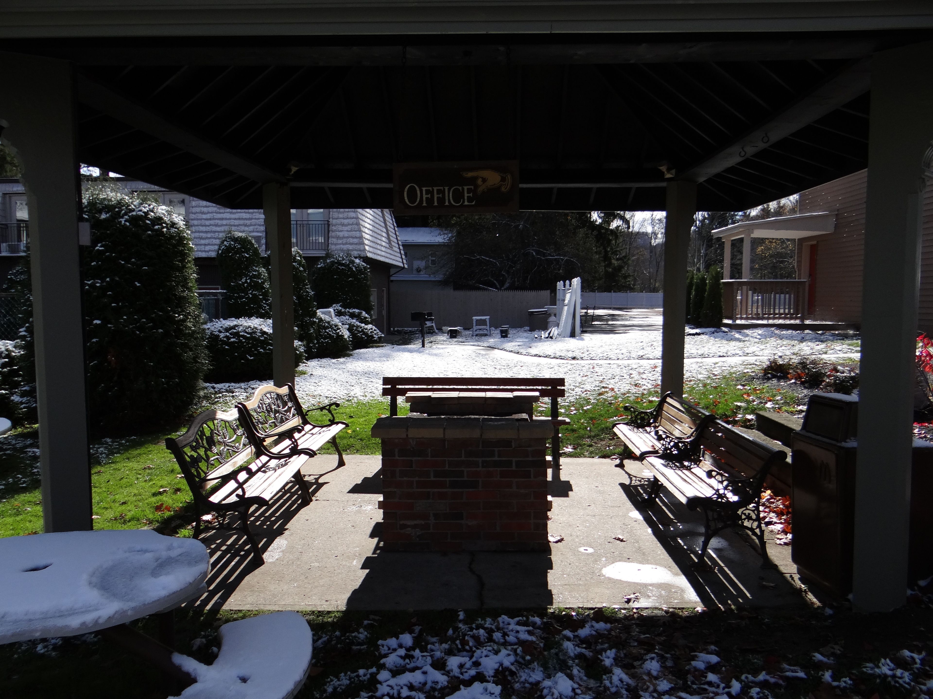 A covered outdoor seating area with benches and a brick table, leading to a building labeled "OFFICE".