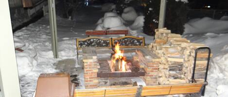 An outdoor fire pit area with a brick fire pit, benches, and a metal grill.