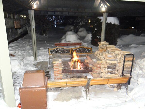 An outdoor fire pit area with a brick fire pit, benches, and a metal grill.