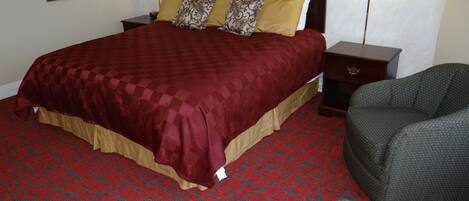 Una habitación de hotel con una cama grande, dos mesitas de noche, una silla y una alfombra estampada.