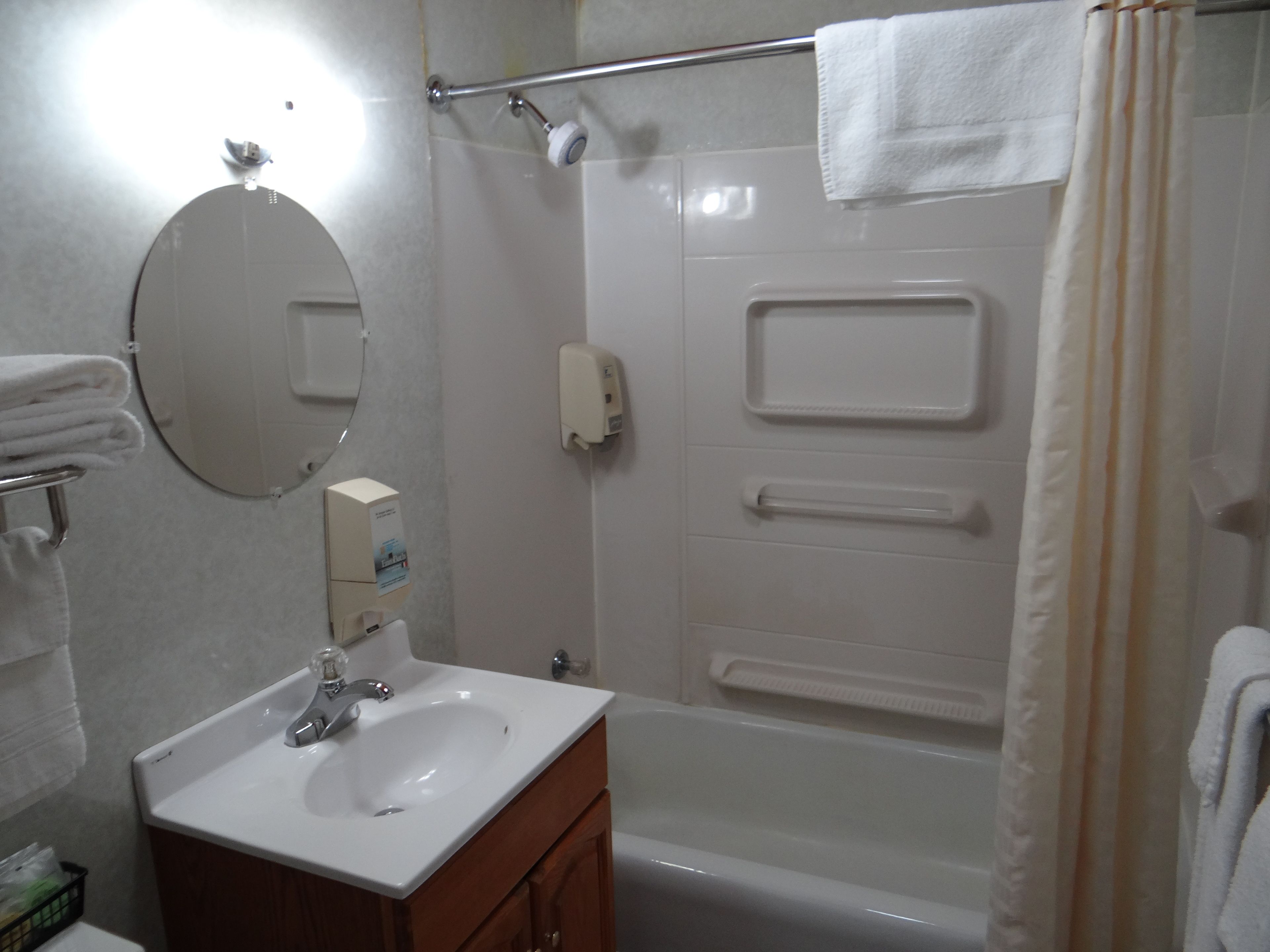 A bathroom with a sink, mirror, towel rack, shower curtain, and a hand dryer.