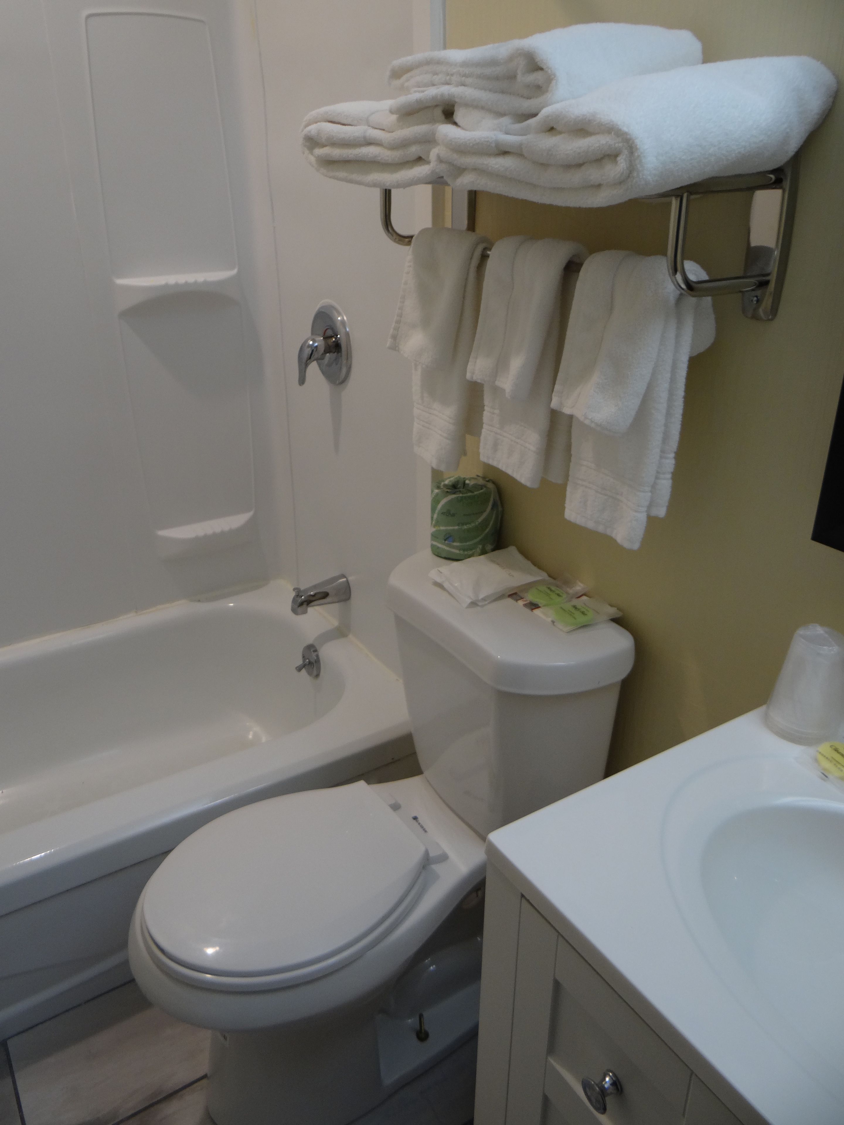 Ein Badezimmer mit Toilette, Waschbecken und Badewanne. Handtücher liegen auf einem Handtuchhalter gestapelt.
