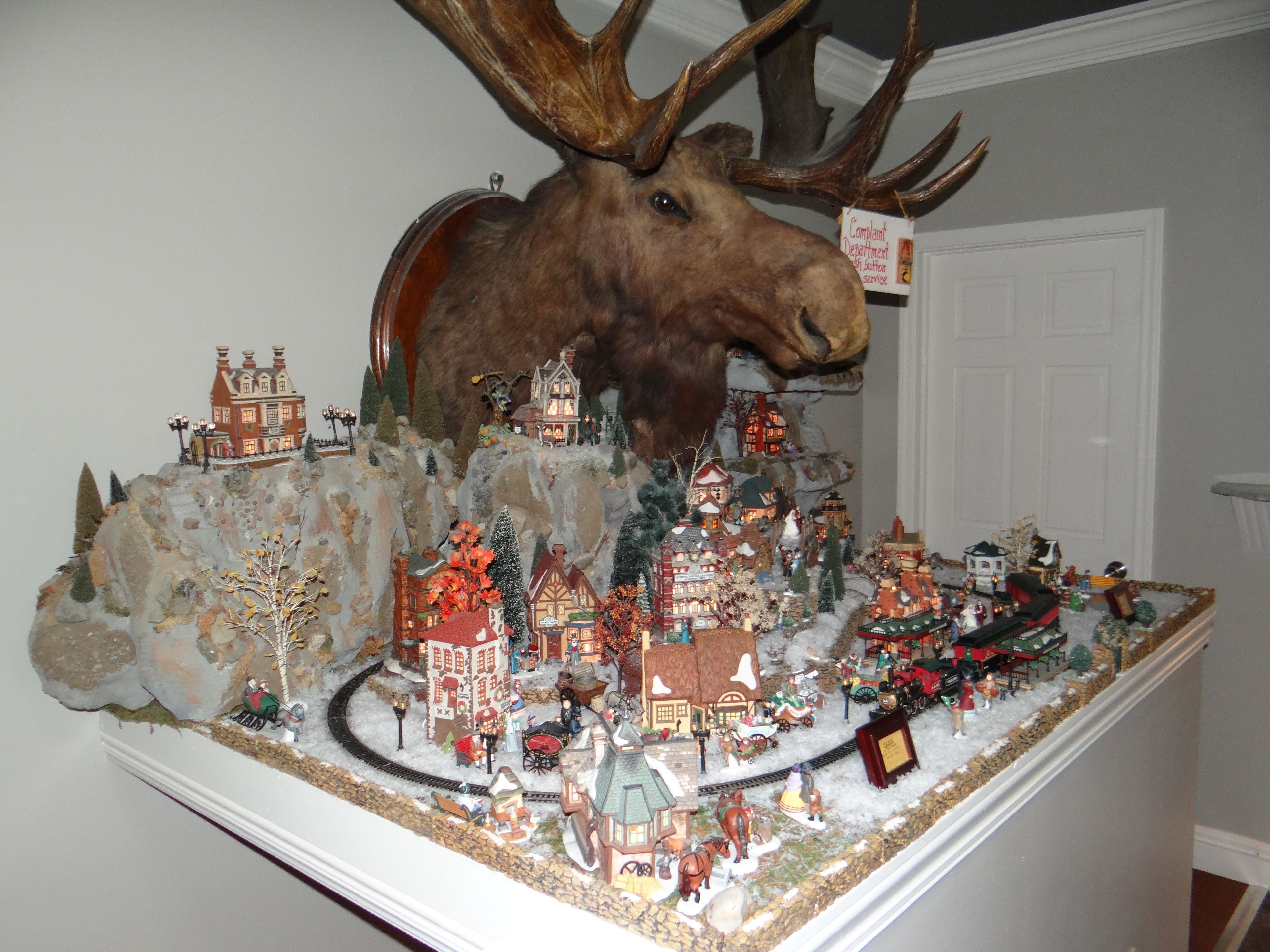 A detailed model train display featuring a moose head, miniature buildings, and various figures.