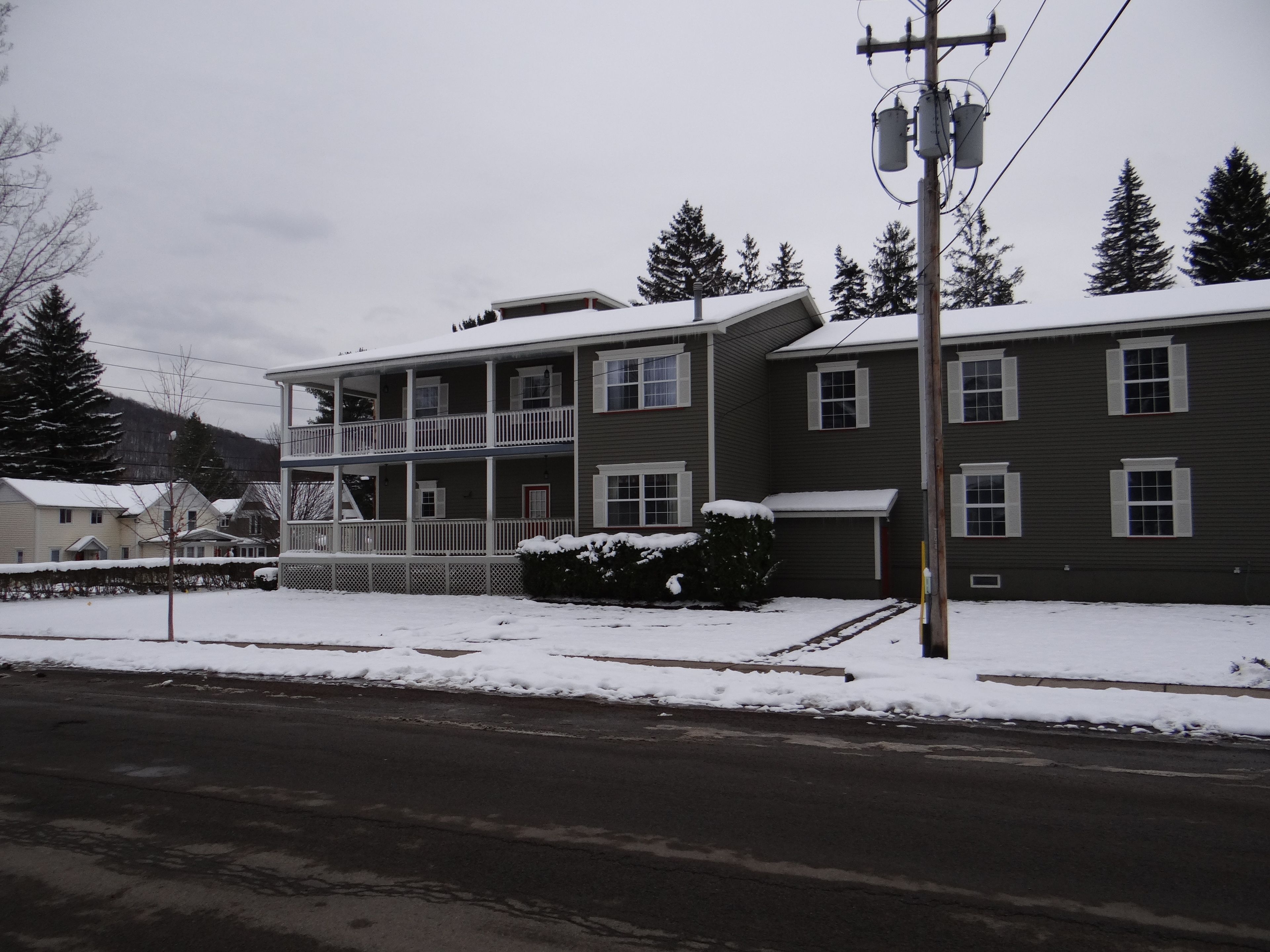 A two-story building with a balcony, a covered front porch, and a snow-covered roof.