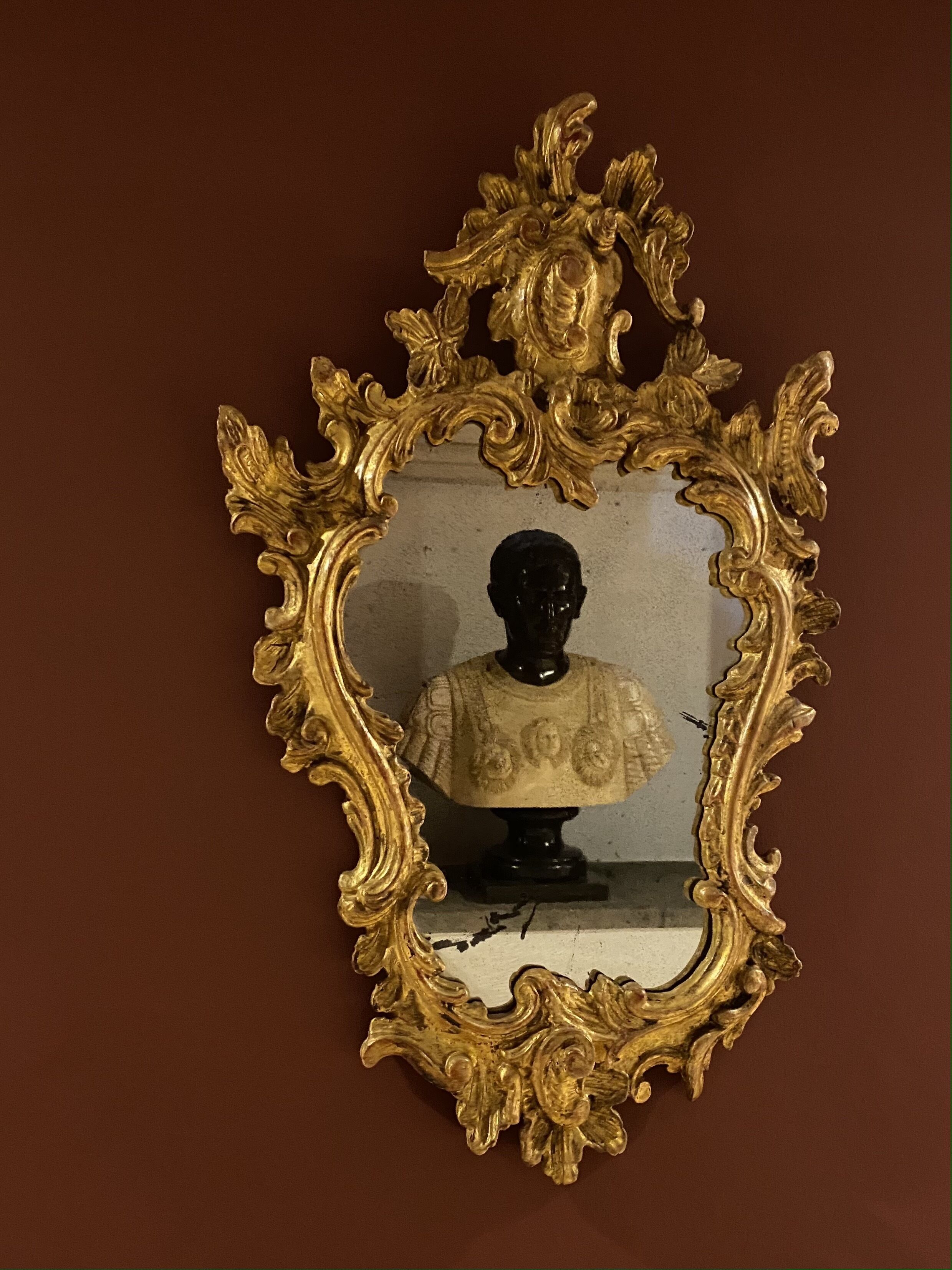 A gold-framed mirror with a bust sculpture in front of it.