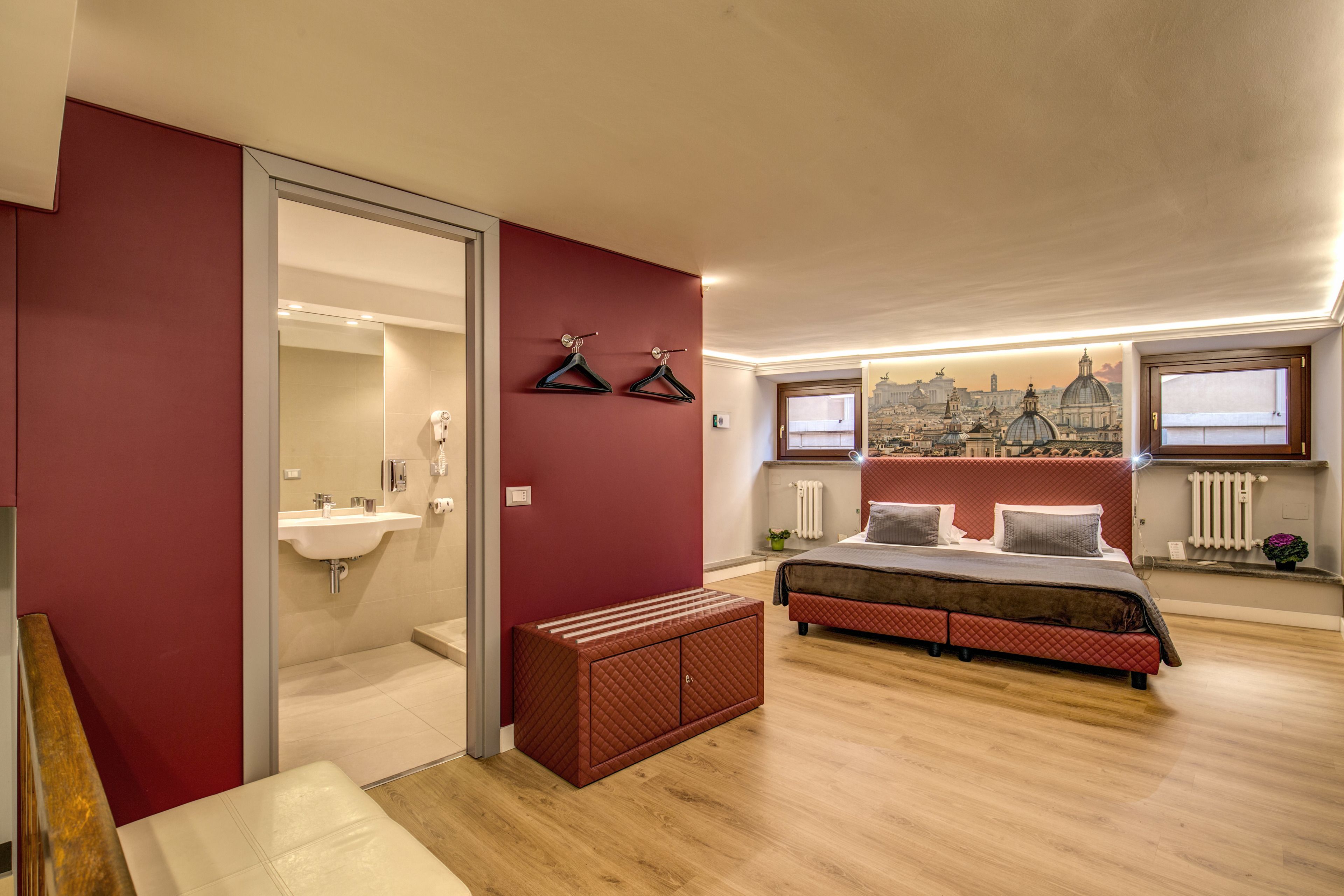 A bedroom with a bed, a bench, a mirror, and a cityscape mural on the wall.
