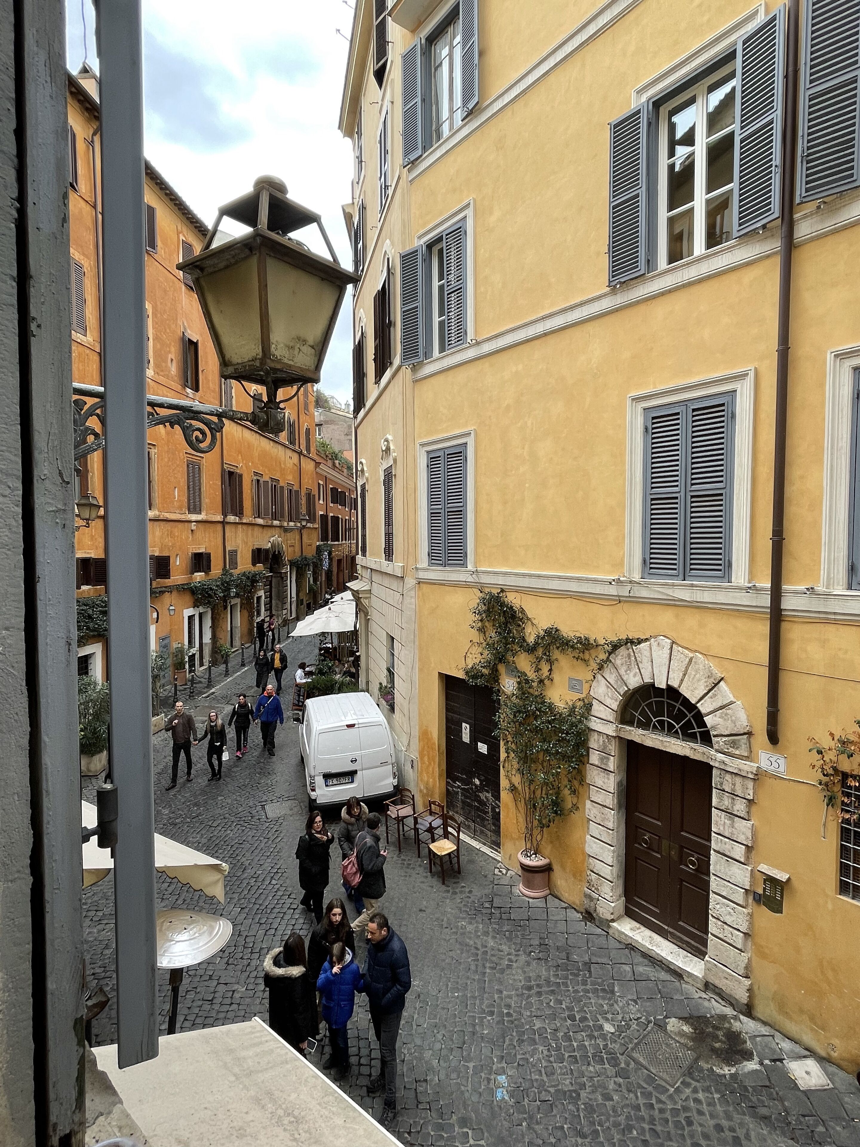 A narrow cobblestone street lined with historic buildings, a white van parked on the side, and people walking.