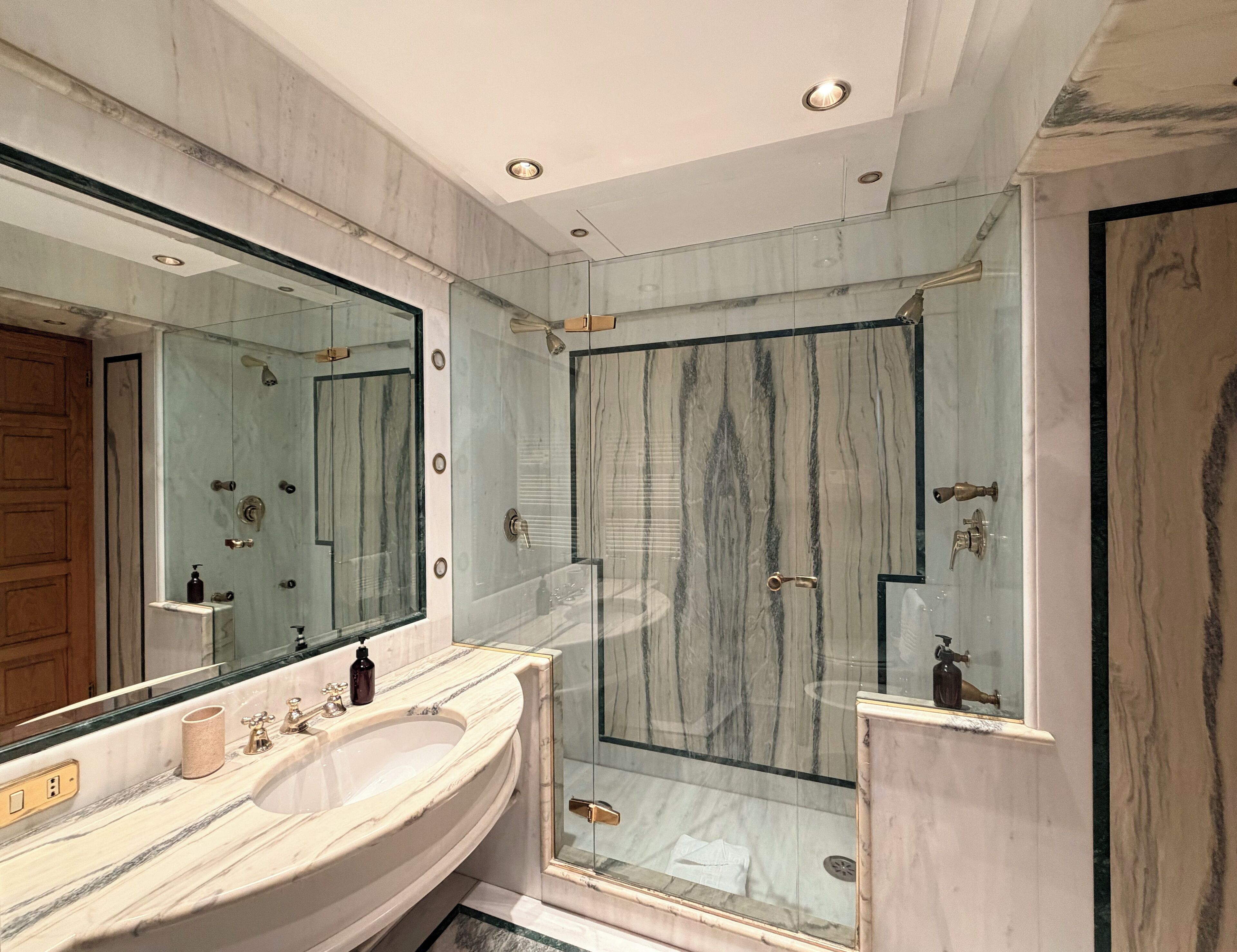 Een badkamer met een marmeren wastafelmeubel, een grote spiegel en een douche met glazen wanden.