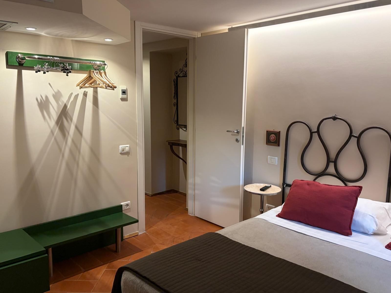 A hotel room with a bed, a bench, a coat rack, and a shower area.