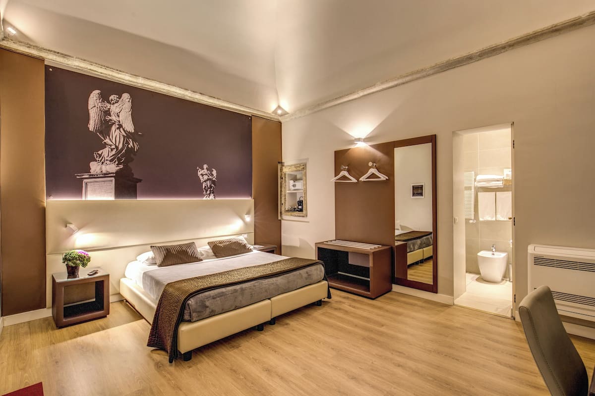 Un dormitorio moderno con una cama grande, mesitas de noche, un tocador, un aparador, un espejo y un baño visible a través de una puerta abierta.