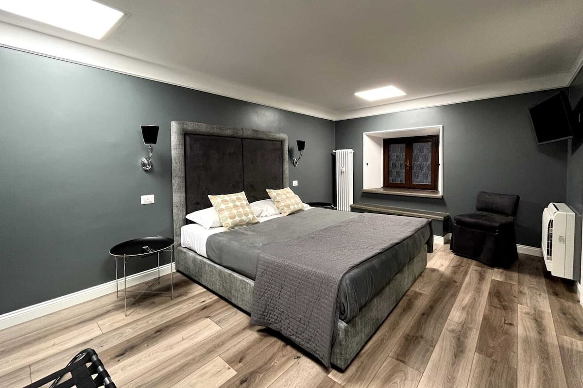 Un dormitorio con una cama grande, una silla, una mesita y un radiador, además de una ventana.