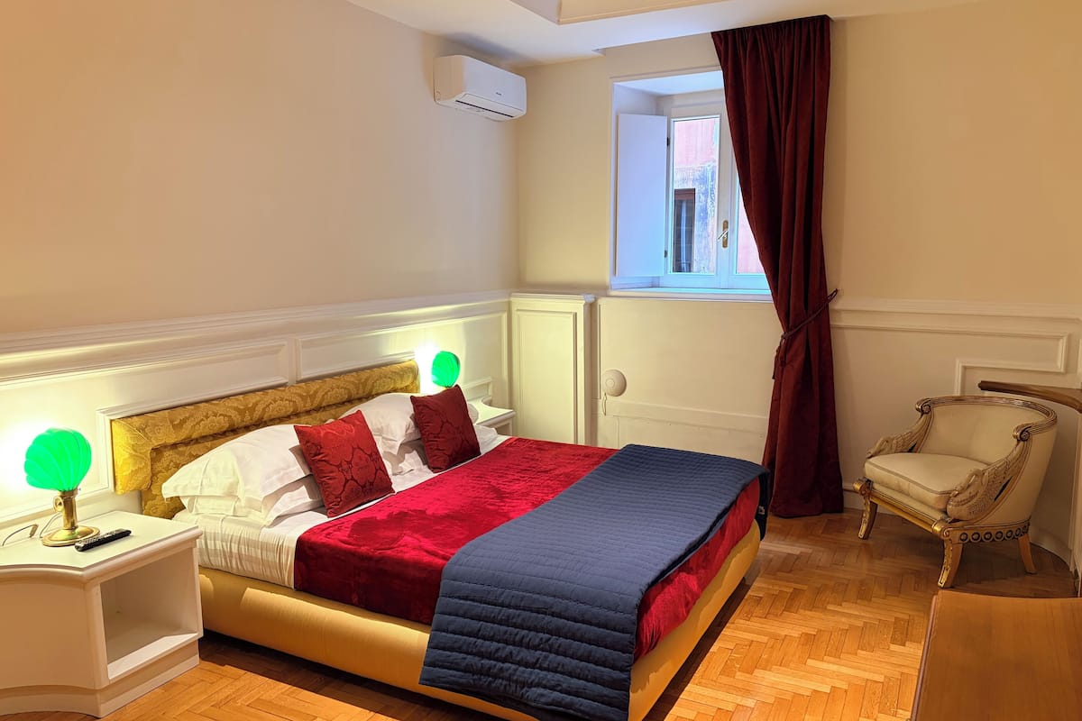 Habitación de hotel ordenada con cama, lámparas de noche, una silla y un ventanal con cortinas.
