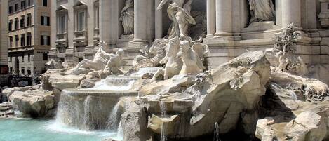 A grand fountain with multiple statues and water features, set against a backdrop of classical architecture.