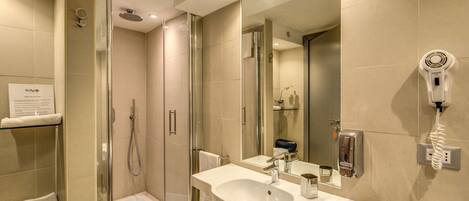 A modern bathroom with a glass-enclosed shower, a large mirror, a sink, and a hairdryer on the wall.