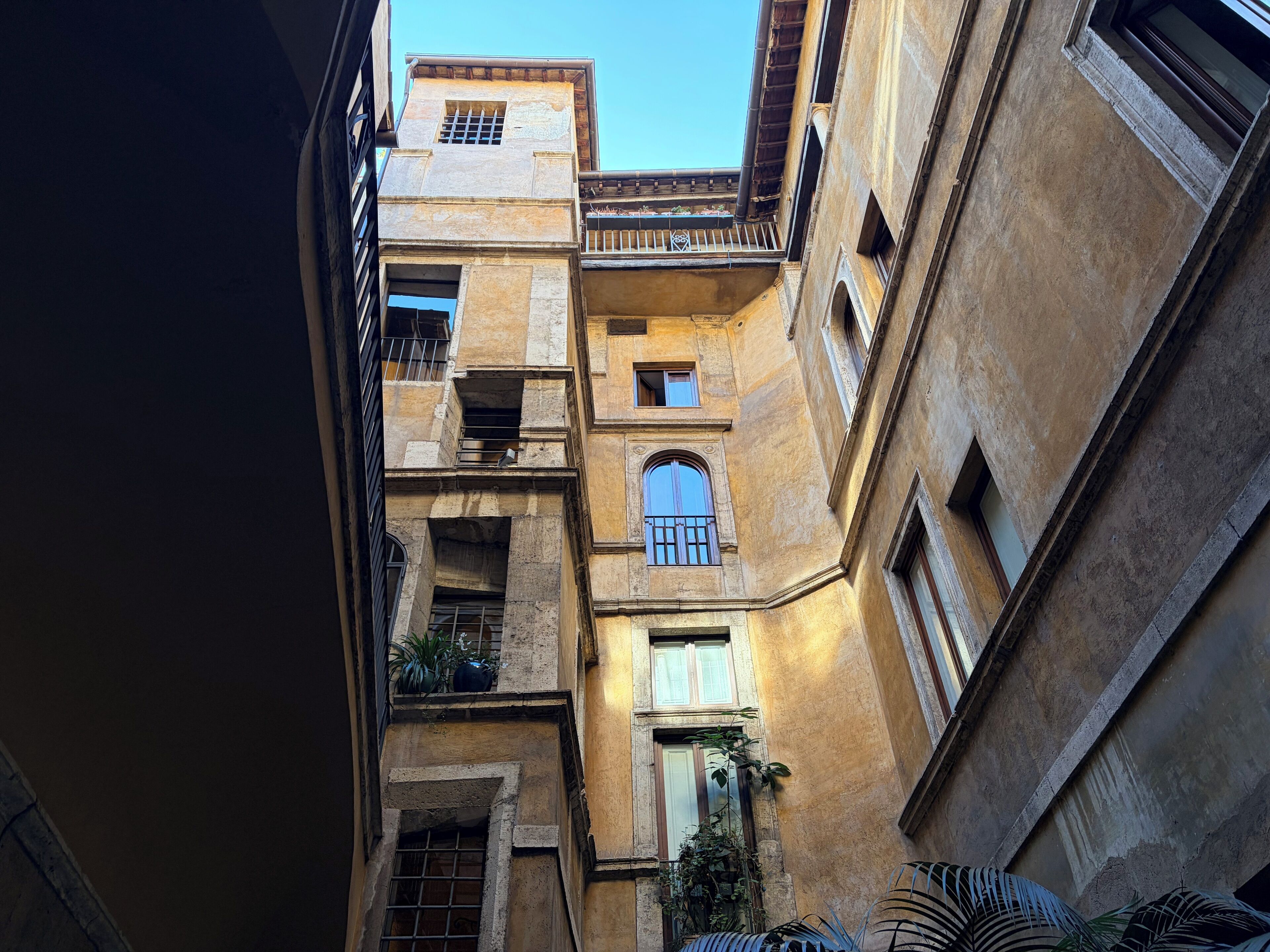 A narrow alleyway between buildings with balconies, large windows, and a mix of stone and plaster facades.