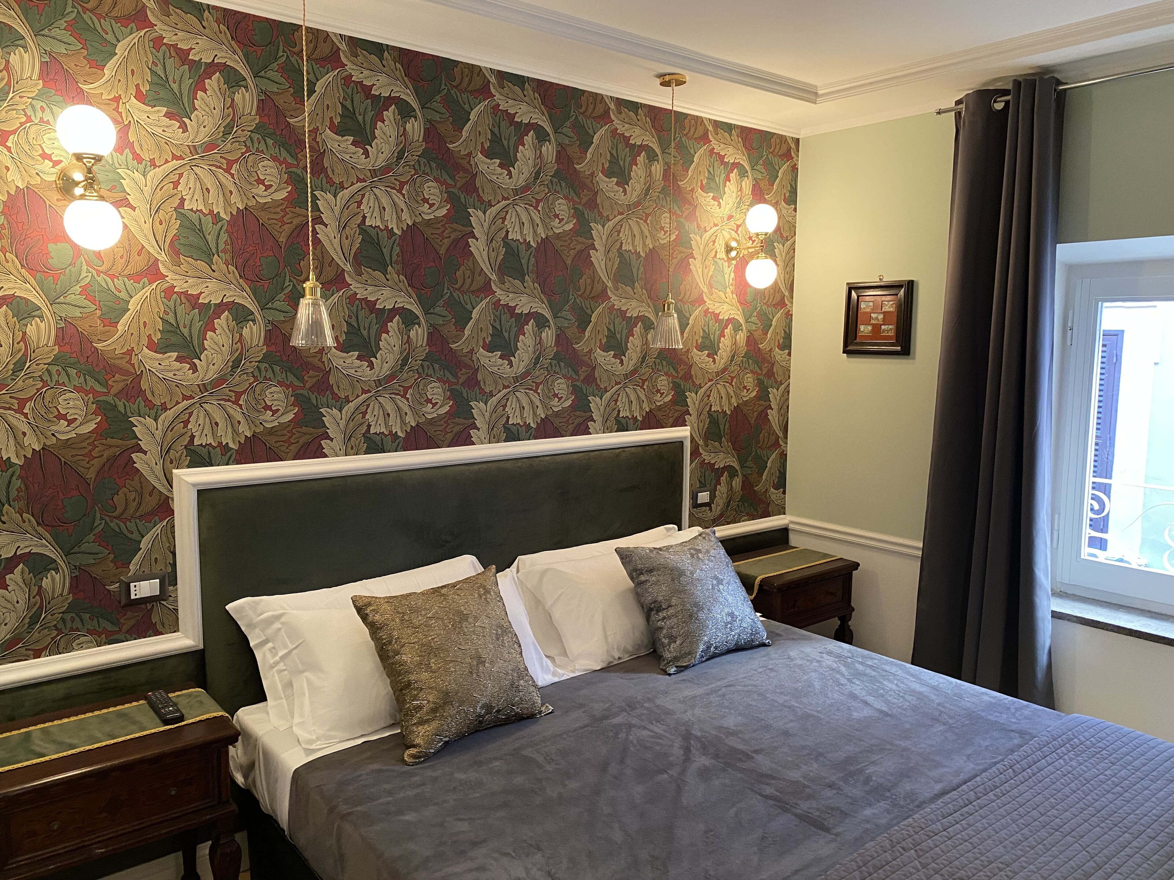 A bedroom with a large bed, two bedside tables, a green headboard, and a floral wallpaper.