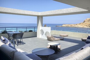 A covered outdoor seating area with a view of the sea, featuring a sofa, chairs, and a small table.