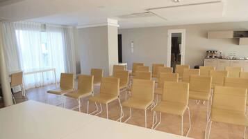 Une salle de conférence avec une longue table et de nombreuses chaises, un coin cuisine et une fenêtre avec des rideaux.