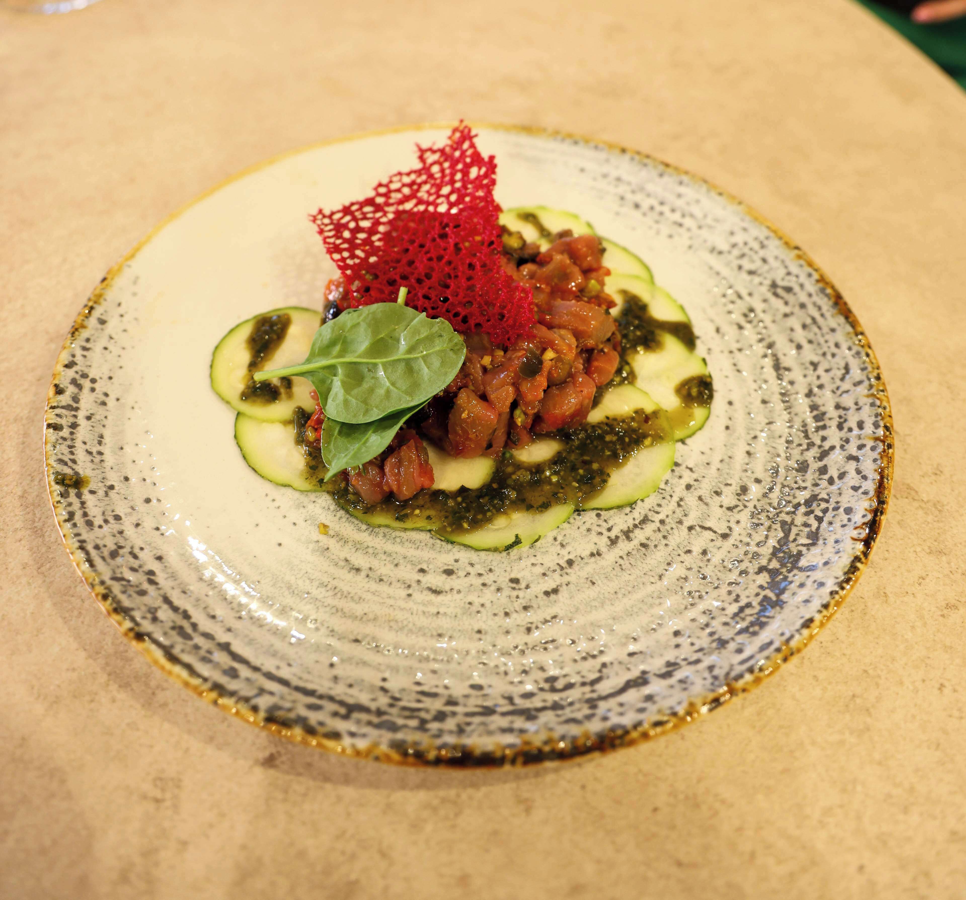 Un plato con un guiso de verduras en rodajas y un detalle decorativo rojo.