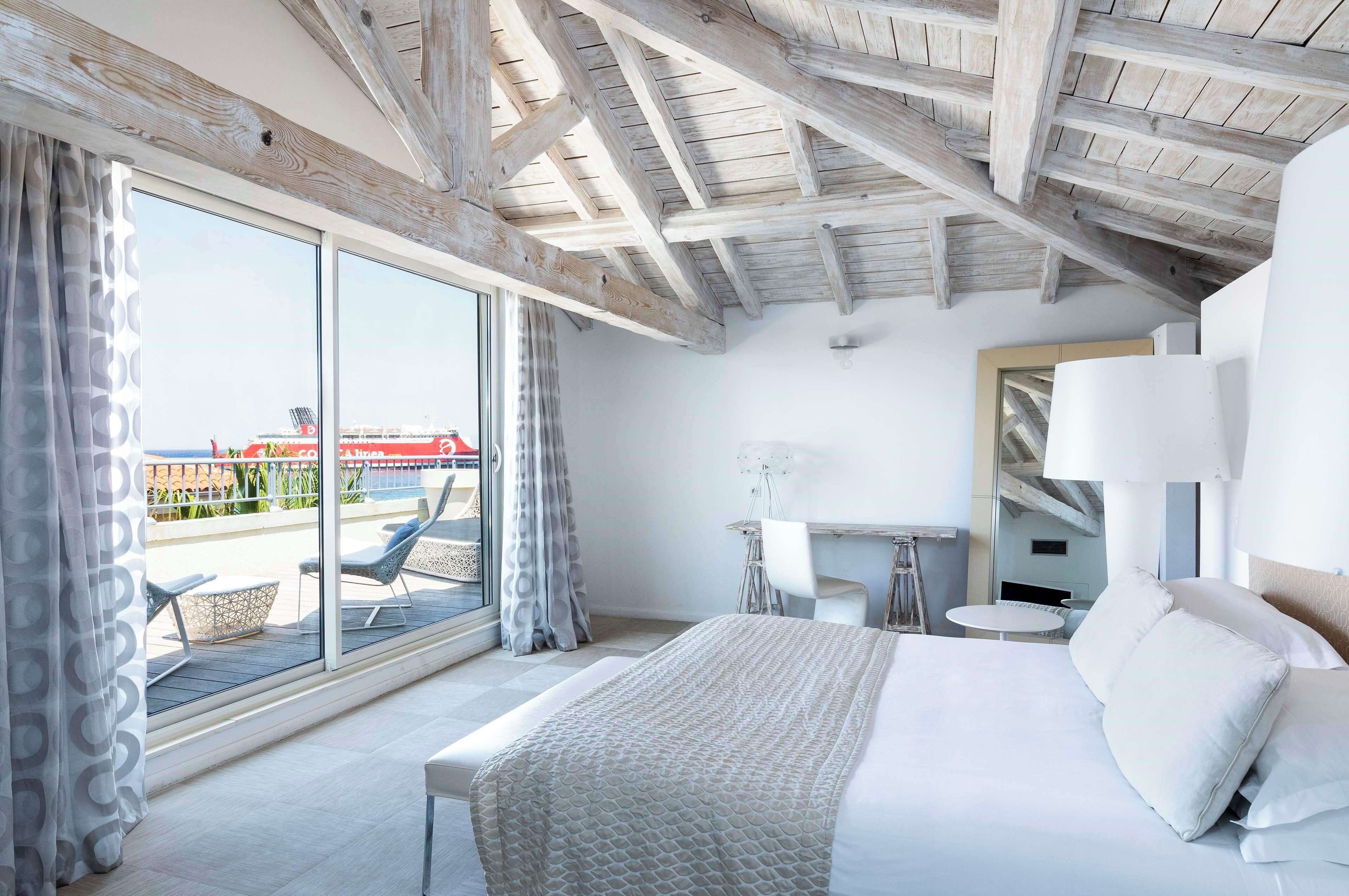A modern hotel room with a large bed, a desk, and a balcony with outdoor seating.