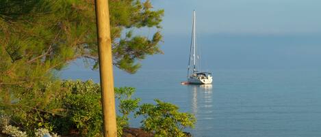 A beachside view with a thatched umbrella, a sailboat, and a white lounge chair.