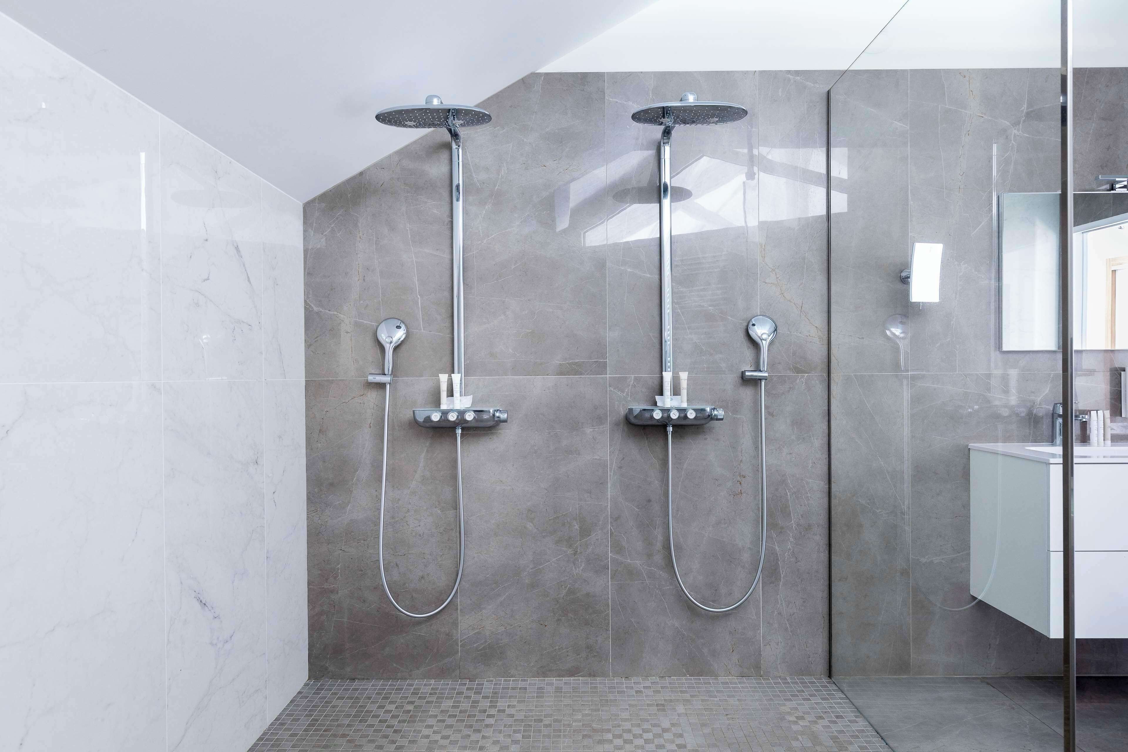 Un baño moderno con dos cabezales de ducha, un box de ducha de vidrio y suelo de baldosas.