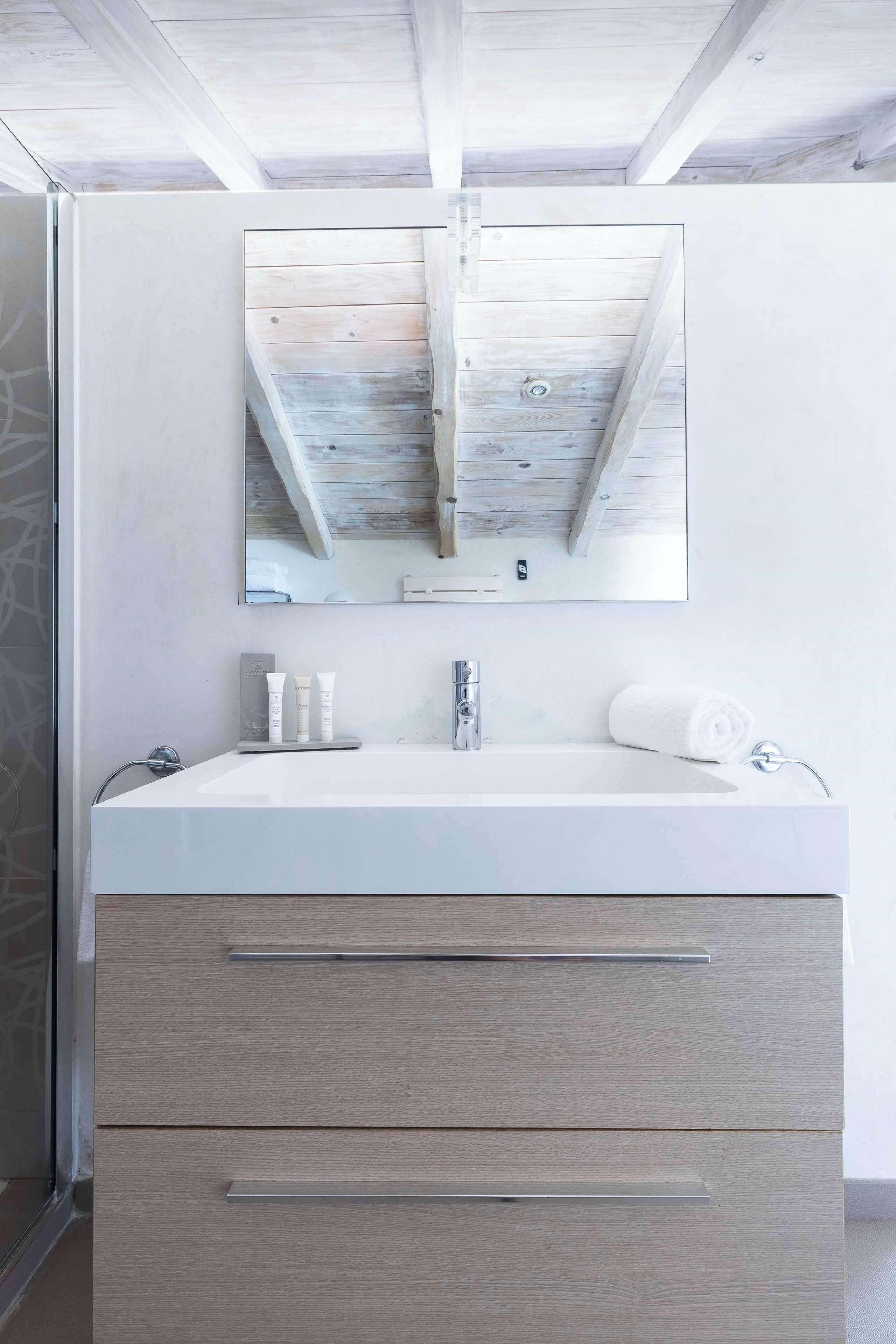Ein Badezimmer mit einem weißen Waschbecken, einem Spiegel und Holzbalken an der Decke.
