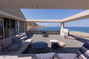 A deck with a sofa, round table, and chairs, overlooking a coastal area.