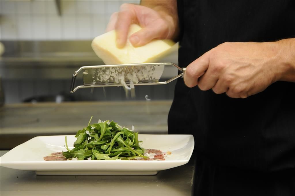 A person grating cheese over a plate of greens.