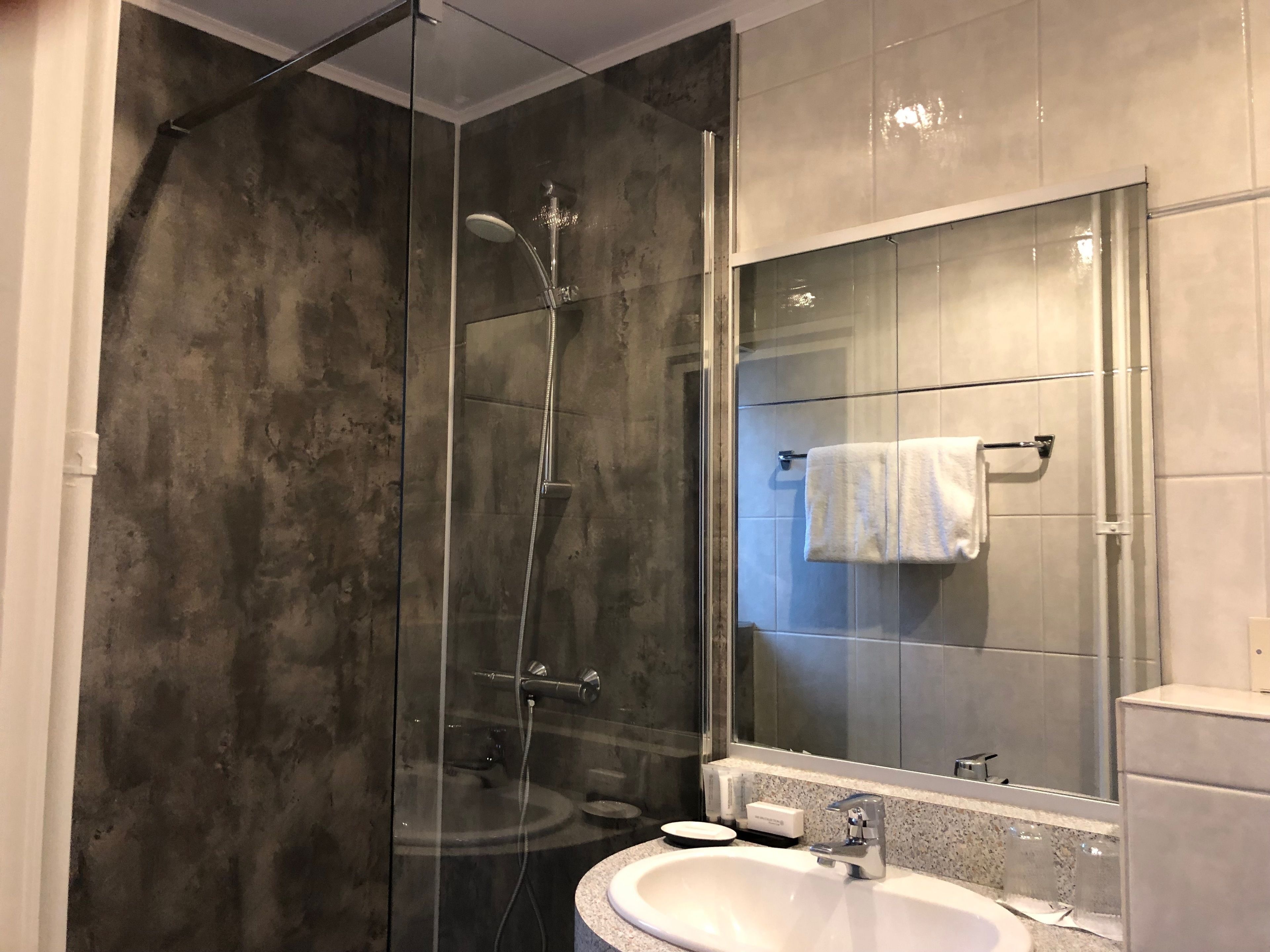 A modern bathroom with a glass-enclosed shower, a white sink, and a large mirror.