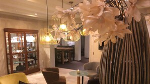 Un salon moderne avec un canapé jaune, un fauteuil marron, un grand vase à rayures et une table en verre sur laquelle est posée une bougie.