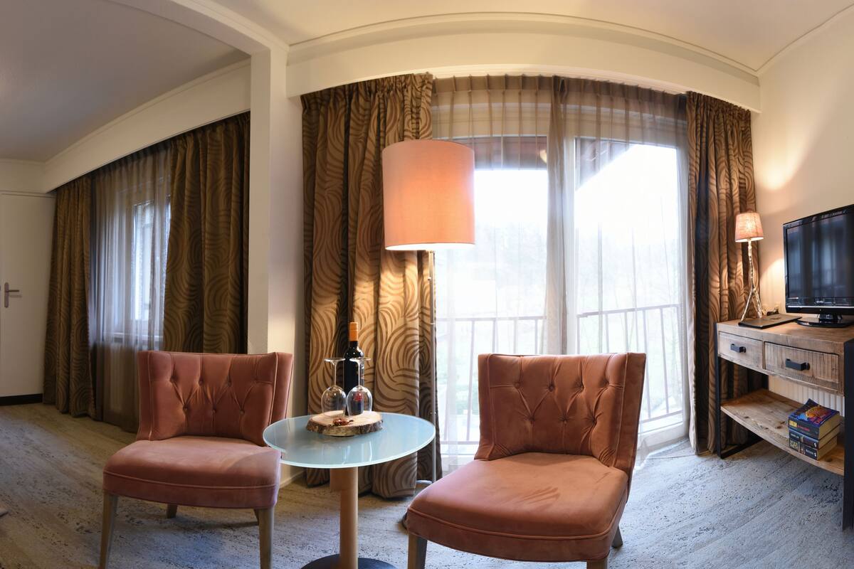 Hotelkamer met een bed, twee fauteuils, een tafeltje, een televisie en gordijnen.