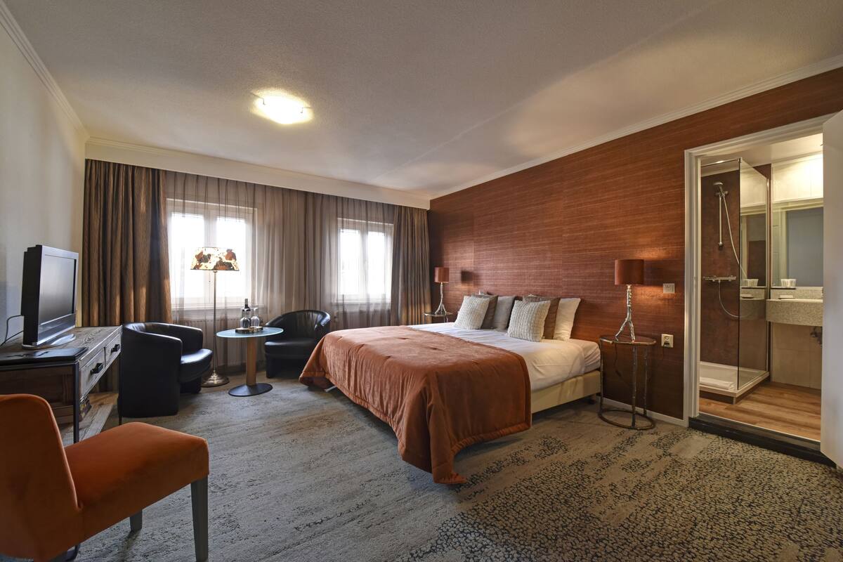 Een hotelkamer met een bed, een bureau met een televisie, een stoel, een klein tafeltje en een badkamer met douche.
