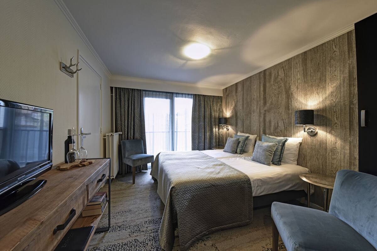 Een moderne hotelkamer met een groot bed, een televisie, een zithoek en uitzicht op het omliggende landschap.
