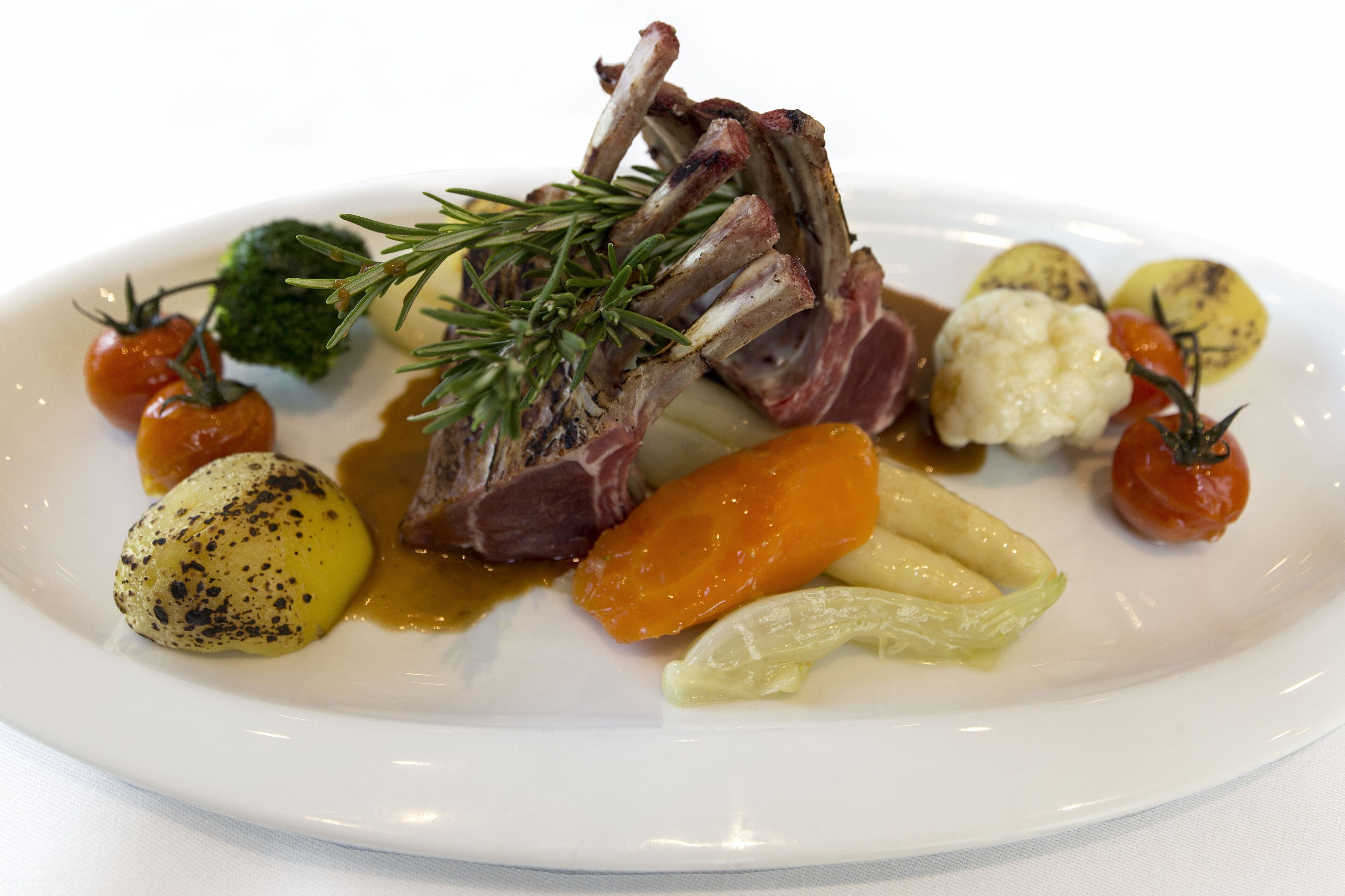 A plate of food with lamb chops, potatoes, carrots, and cherry tomatoes.