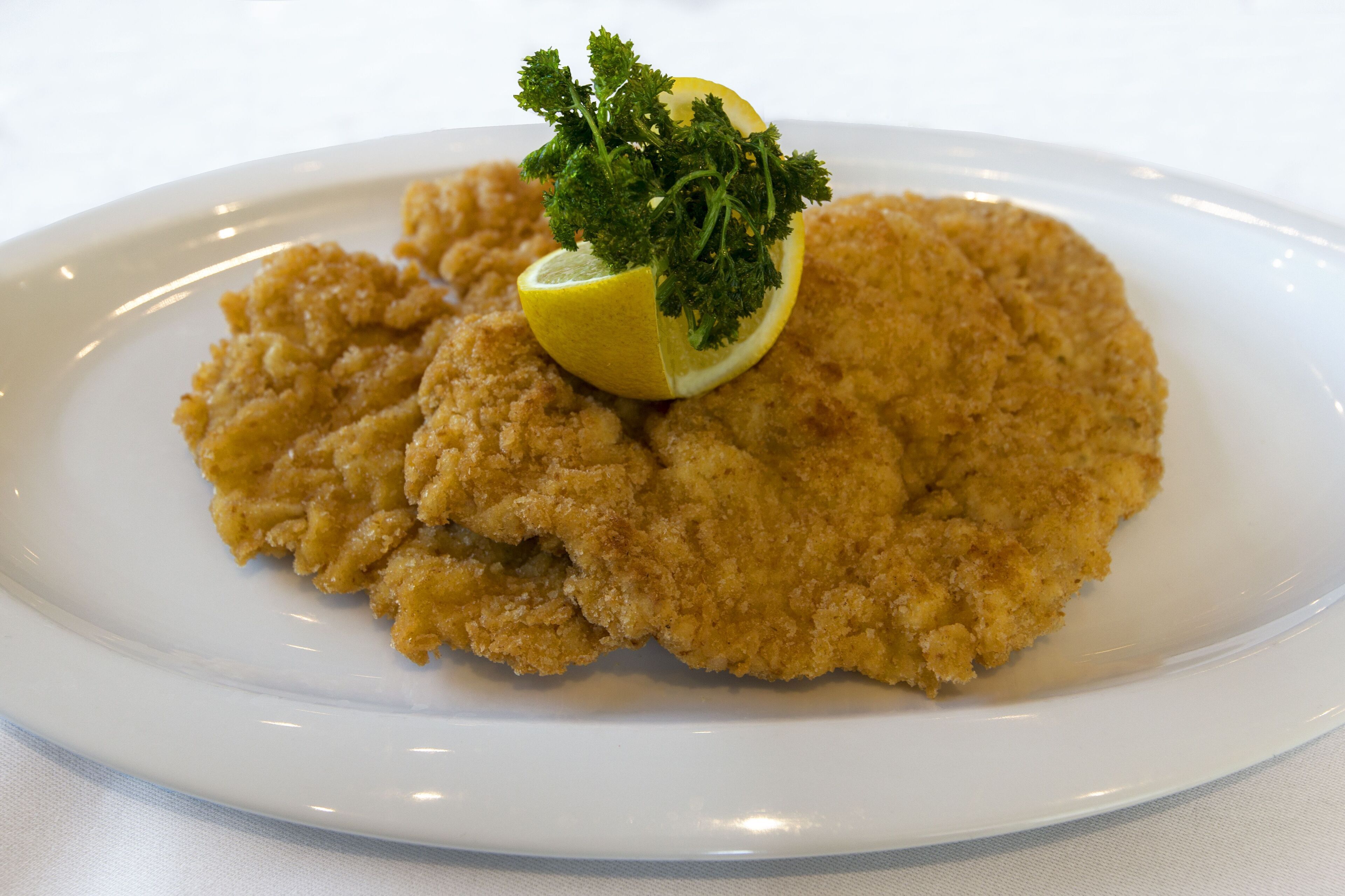 Un plato blanco con una milanesa, una cuña de limón y perejil picado.
