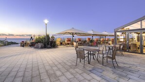 Un espace extérieur aménagé en terrasse, avec des tables et des chaises, un lampadaire et une vue sur la mer.
