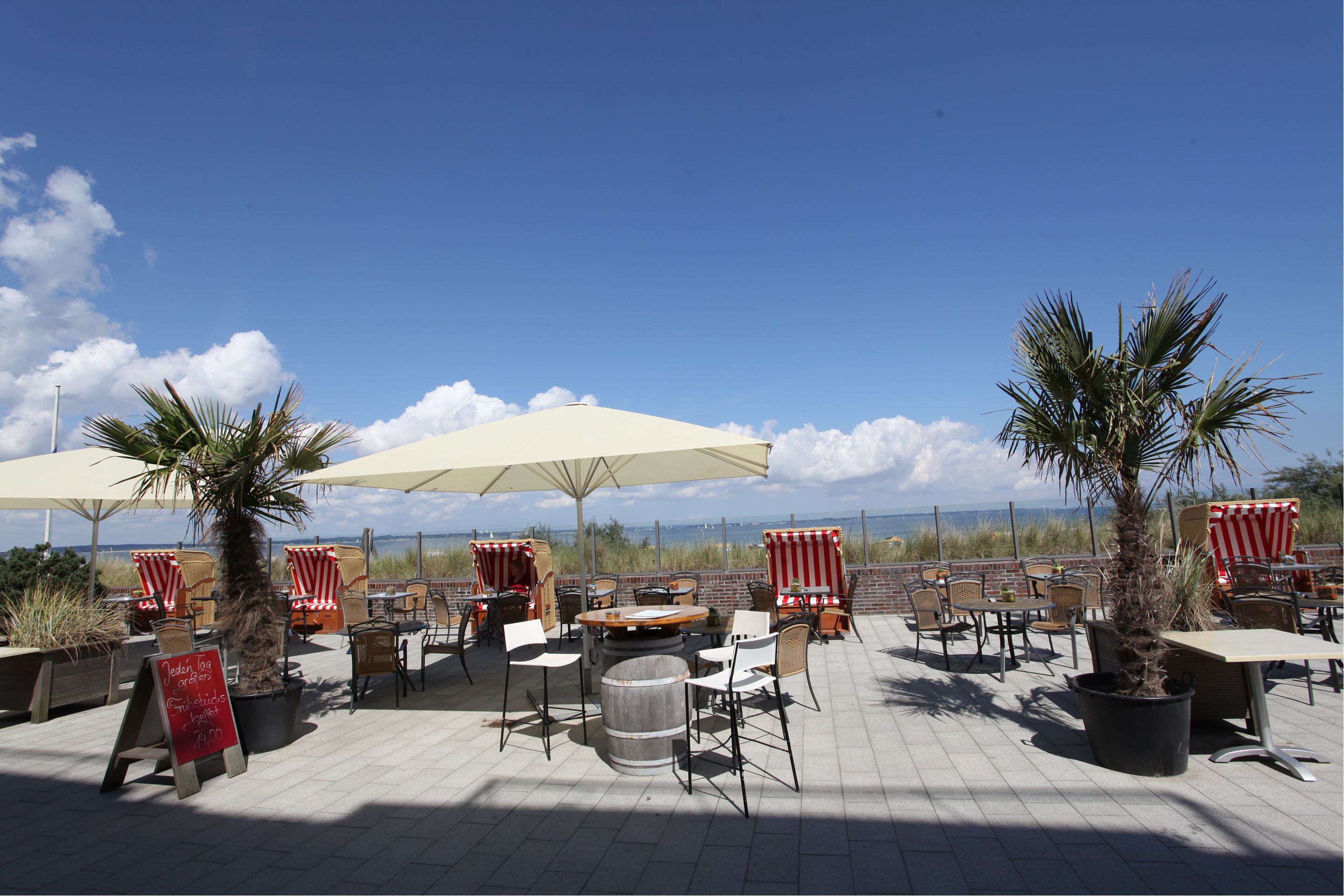 An outdoor patio area with tables and chairs, umbrellas, and potted plants.