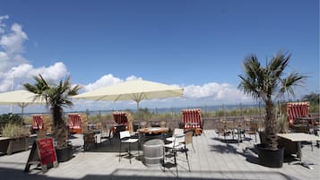 An outdoor patio area with tables and chairs, umbrellas, and potted plants.