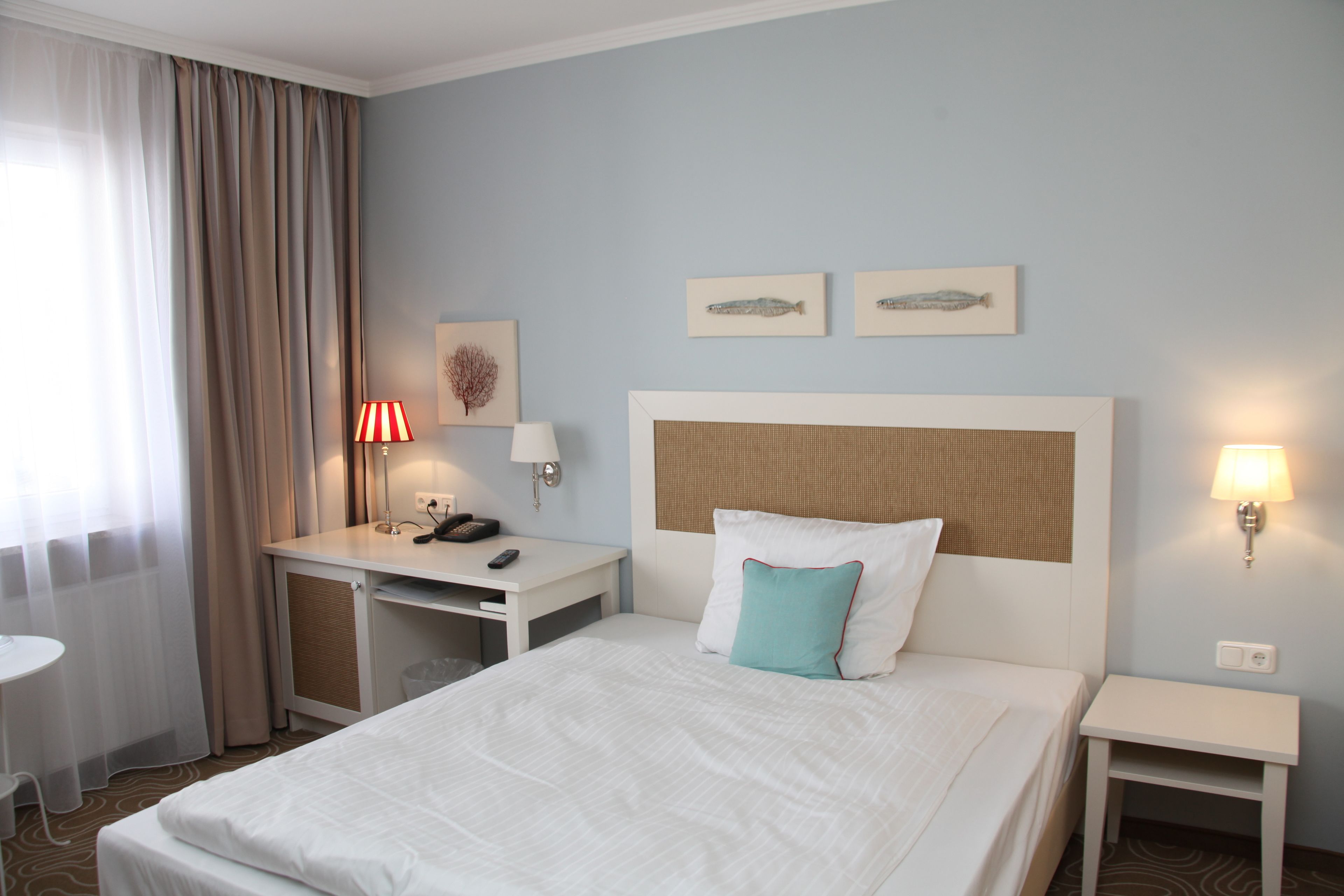 A hotel room with a bed, a desk, a chair, a lamp, and two wall-mounted lamps.