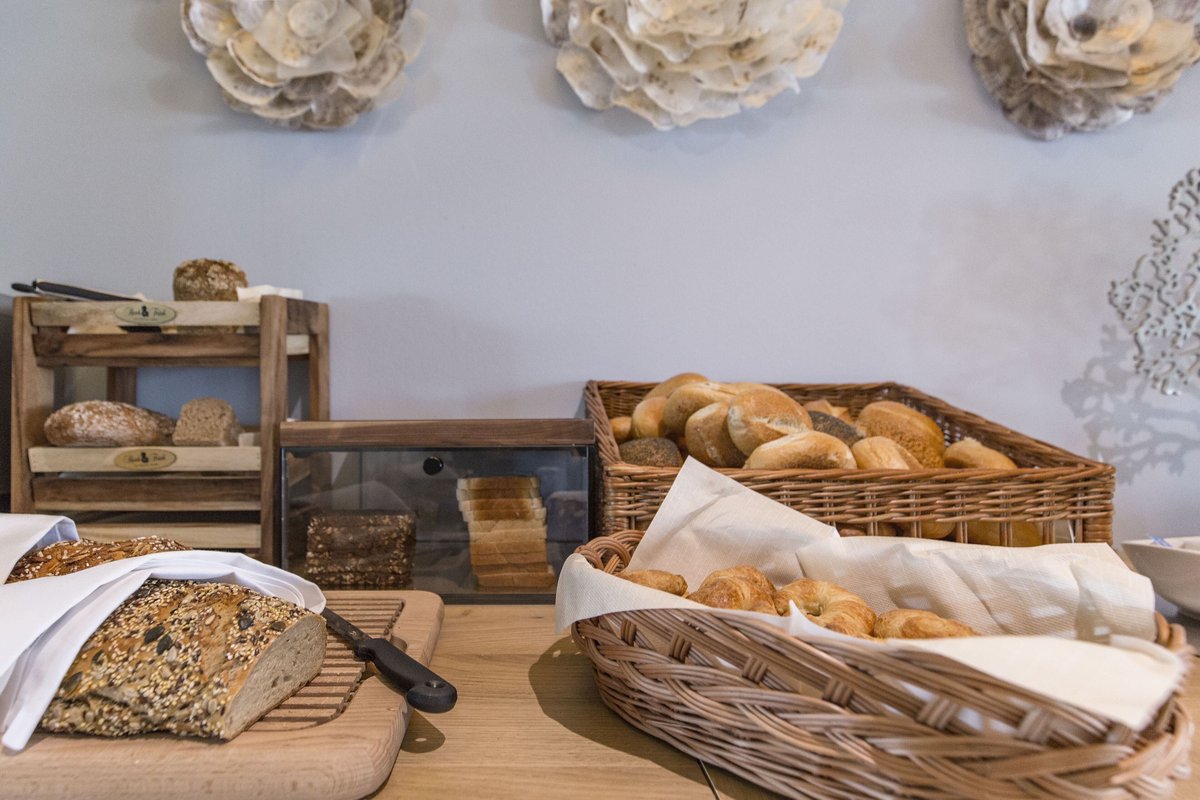 A bakery display with various breads and pastries, a cutting board with a knife, and a wicker basket with croissants.
