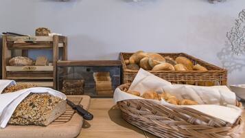 A bakery display with various breads and pastries, a cutting board with a knife, and a wicker basket with croissants.