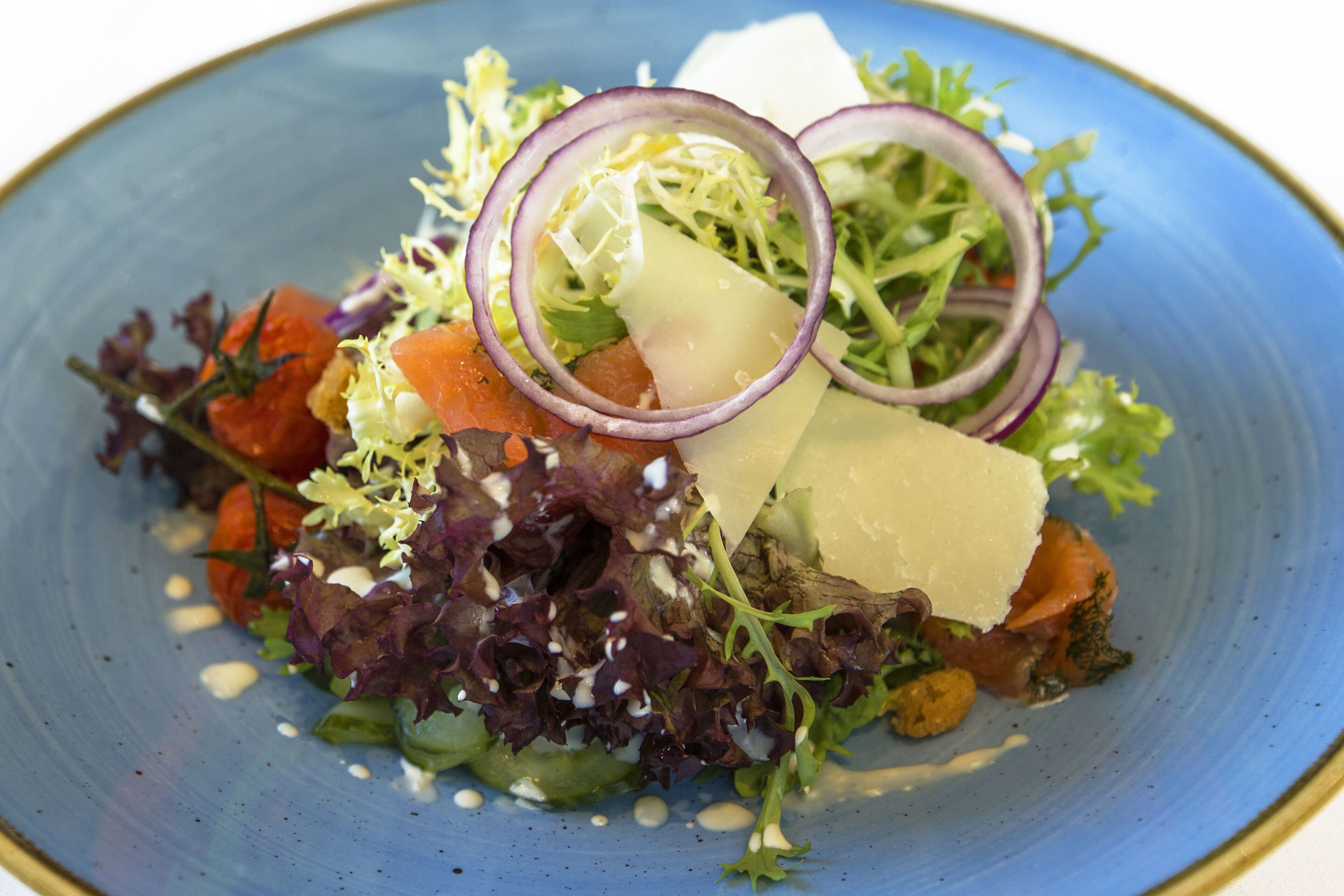 Ein blauer Teller mit einem Salat aus verschiedenen Gemüsesorten und Käse.