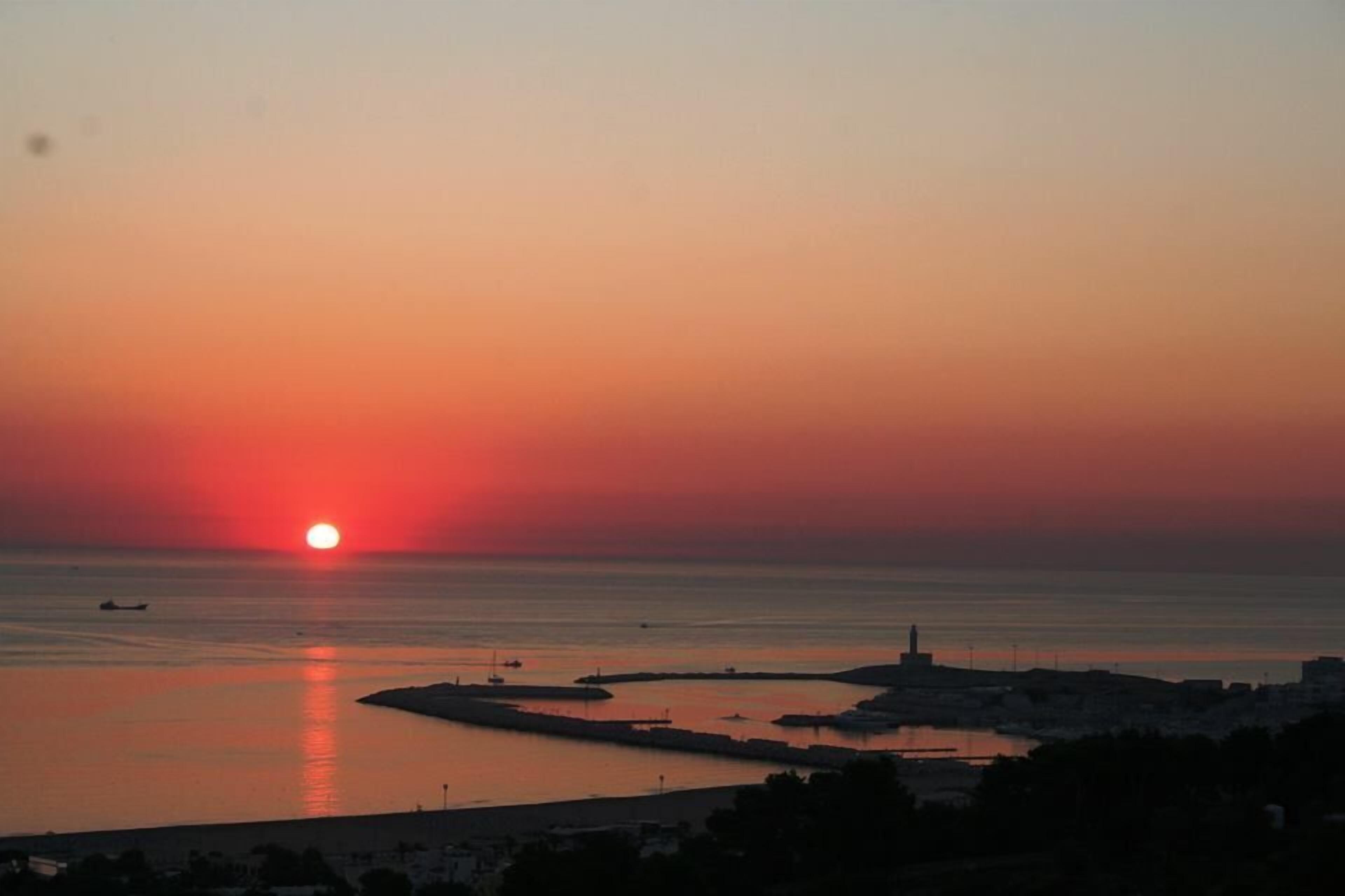 A sunset over a coastal area with a lighthouse and marina.